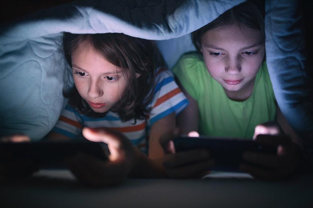 dzieci z telefonami w dłoni pod kołdrą